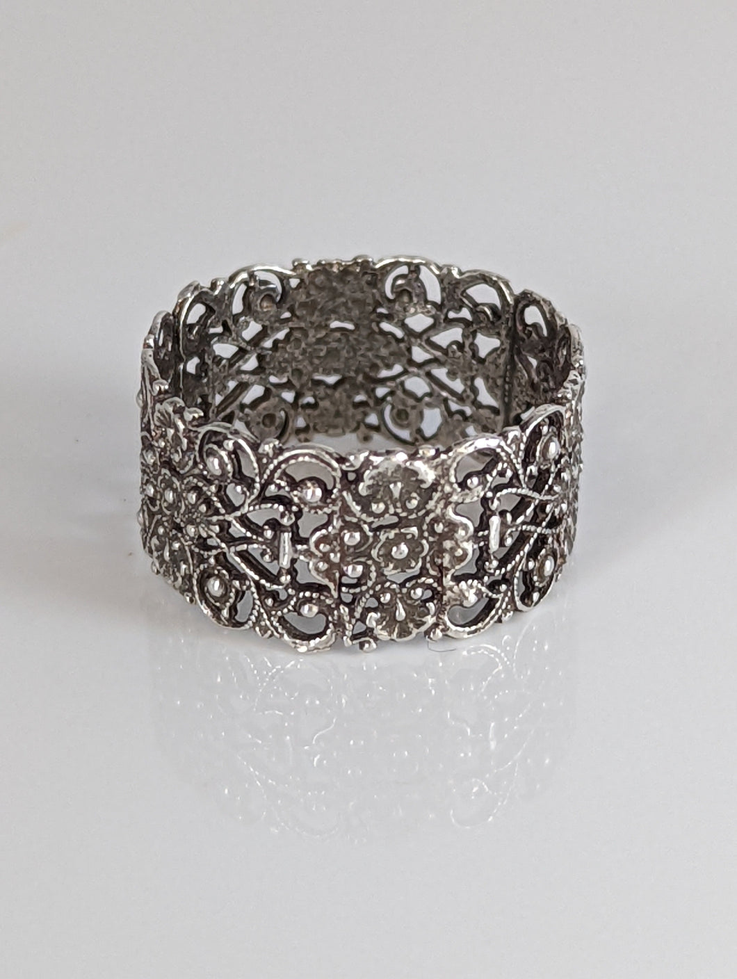A silver filigree band ring with a detailed, intricate pattern.